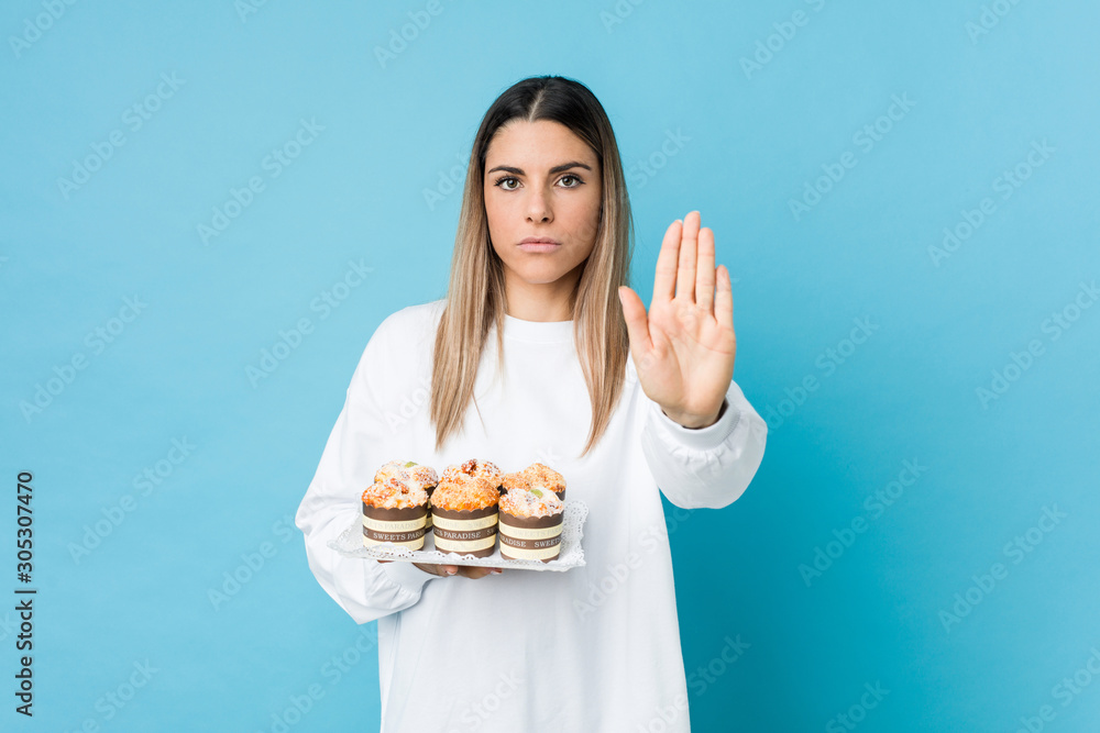 Young caucasian woman holding a sweets cake standing with outstretched hand showing stop sign, preventing you. Young caucasian woman holding a sweets cake standing with outstretched hand showing stop sign, preventing you.