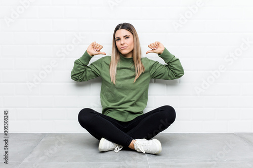 Young caucasian woman sitting on the floor feels proud and self confident, example to follow.