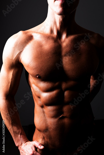A man demonstrates a beautiful athletic torso. In contrasting light. With shine and water.