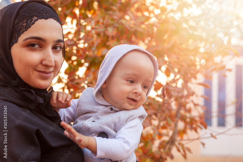 Young Muslim woman in hijab holding her 1-year-old baby boy, hugging and kissing. Happy Muslim mother in abaya clothing kiss and play with her little child Young Muslim woman in hijab holding her 1-year-old baby boy, hugging and kissing. Happy Muslim mother in abaya clothing kiss and play with her little child