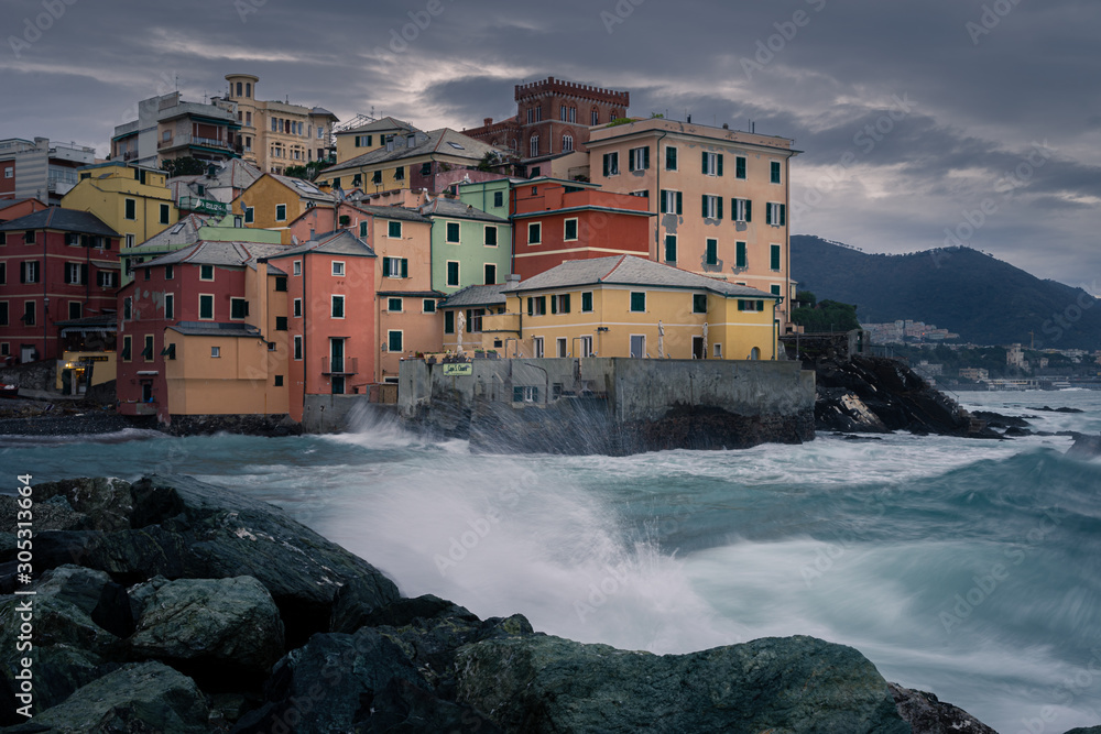 Genoa, Italy. Ancient fishing village during the storm. In the foreground, waves breaking on the rocks. Gloomy sky. Dramatic atmosphere