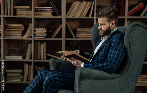 Elegant man in a suit sitting in vintage room and reading book. Fashion man.