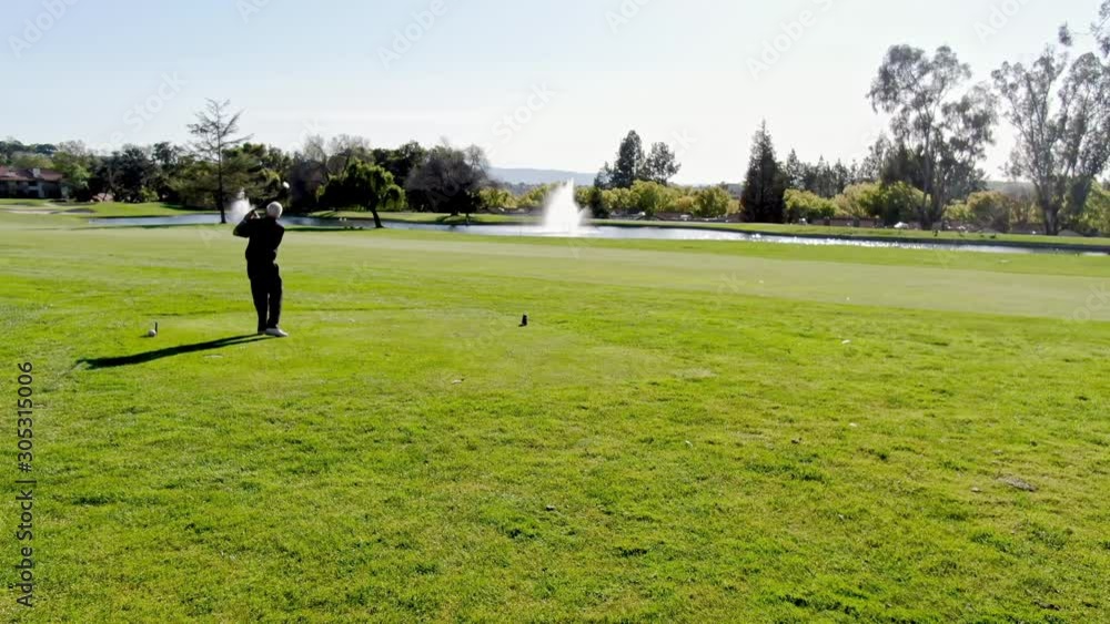 Arial: Handsome older golfer swinging and hitting golf ball on beautiful course Arial: Handsome older golfer swinging and hitting golf ball on beautiful course