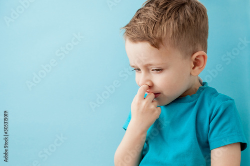 Little caucasian boy picking his nose on blue background