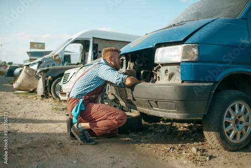 Mechanic stuck head under the hood, car junkyard