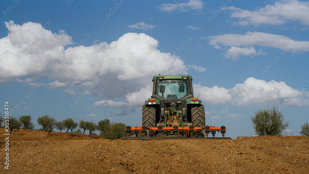 Fototapeta premium Tractor verde labrando un campo de almendros con nubes