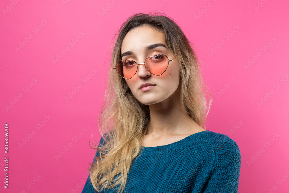 Romantic blonde-haired girl in trendy heart glasses posing with shy smile. Studio close-up portrait on a pink background. Romantic blonde-haired girl in trendy heart glasses posing with shy smile. Studio close-up portrait on a pink background.