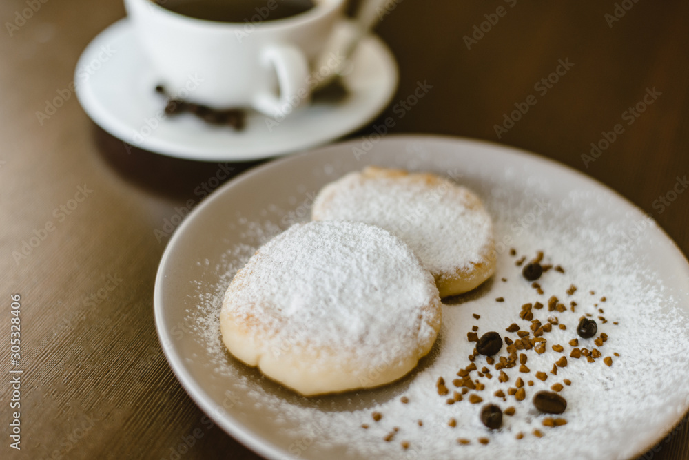 Cheesecakes with icing sugar on a plate on the background of freshly brewed coffee. Wrong tasty sweet sugar breakfast Cheesecakes with icing sugar on a plate on the background of freshly brewed coffee. Wrong tasty sweet sugar breakfast