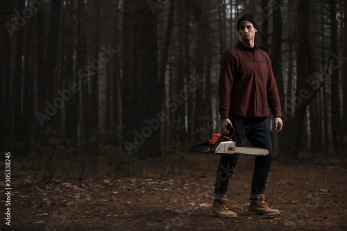 Lumberman working with chainsaw in the forest. Strong lumberjack with the chainsow in the forest.Stylish lumberman getting ready for work. Lifestyle.