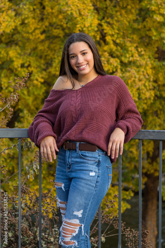 mixed raced teenage girl leaning against railing with yellow fall leaves in the background