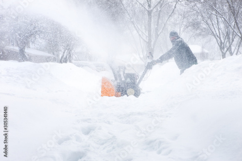 Man using a snowblower to clear his sidewalk and driveway, low visability photo