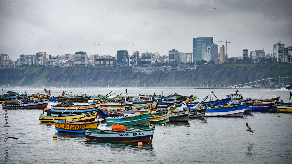 Lima, Peru - Nov 17, 2019: Fishing boats in Chorrilos harbour against the backdrop of the commerical Miraflores district