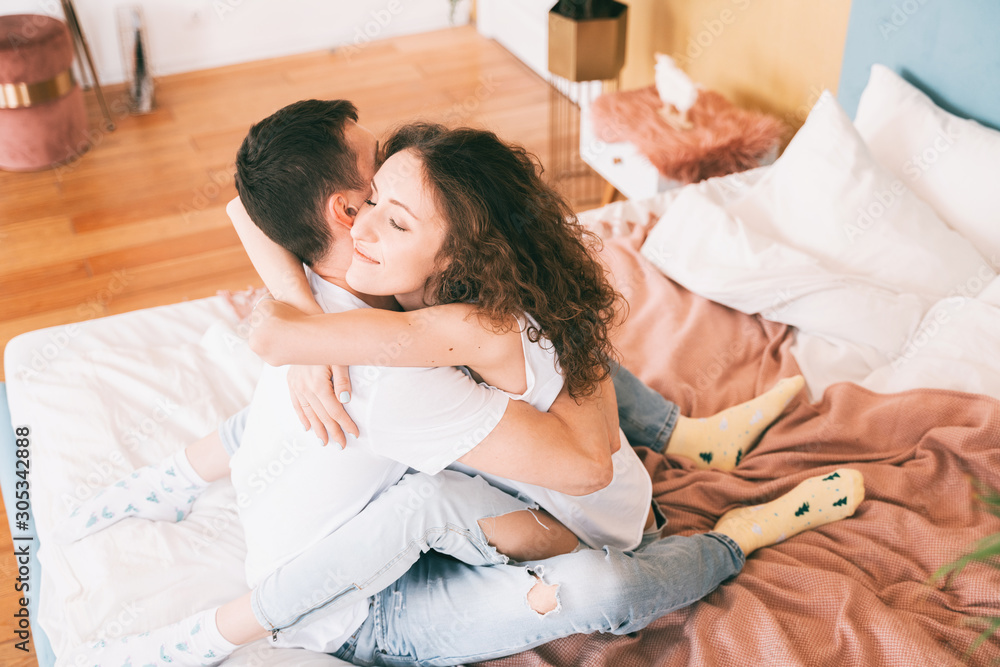 Happy young couple tenderly hugging on the bed in the bedroom, romantic time together concept.