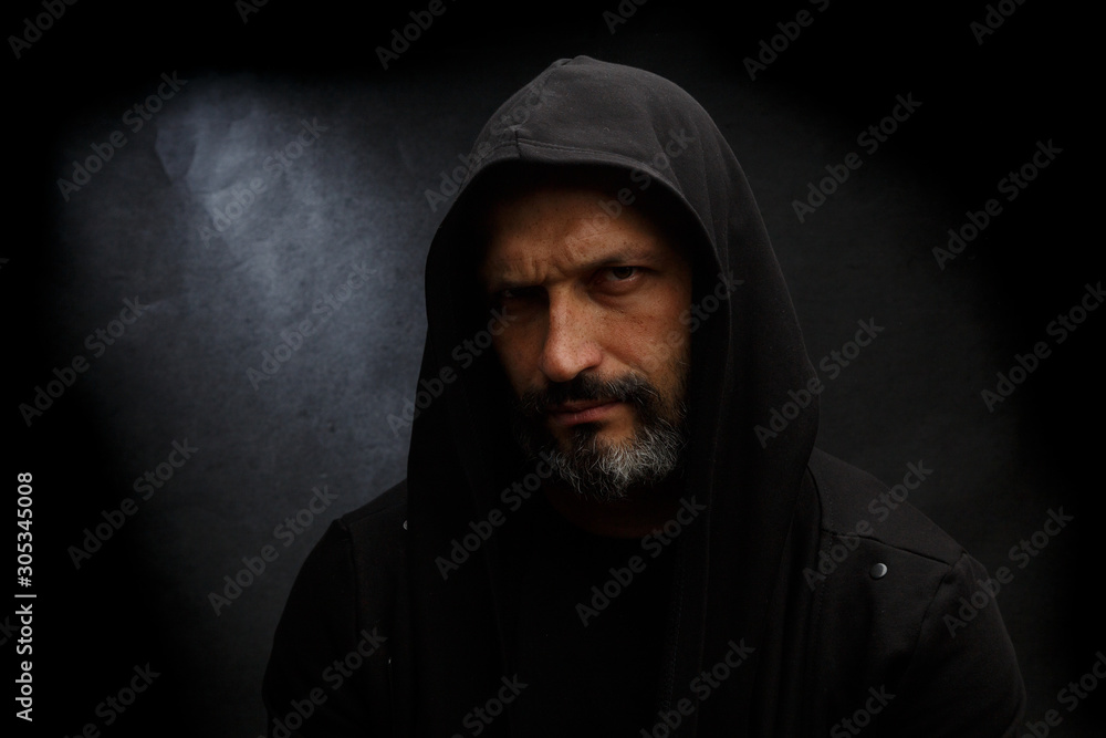 Portrait of a bald man with a beard in a black hood on a dirty gray background. Portrait of a bald man with a beard in a black hood on a dirty gray background.