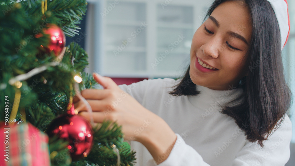 Asian women decorate Christmas tree at Christmas festival. Female teen happy smiling celebrate xmas winter holidays in living room at home. Close up shot. Asian women decorate Christmas tree at Christmas festival. Female teen happy smiling celebrate xmas winter holidays in living room at home. Close up shot.