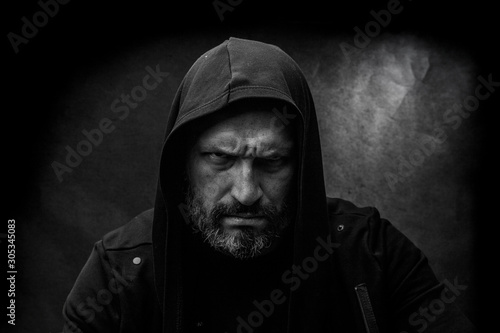 Black and white portrait of a bald bearded man in a hood on a dirty gray background