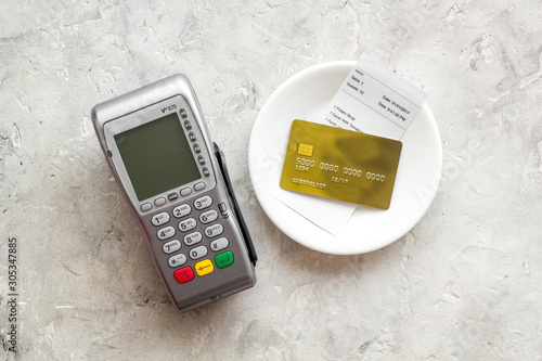 Electronic payments in restaurant. Bank card near aquiring terminal and bill on grey background top view photo