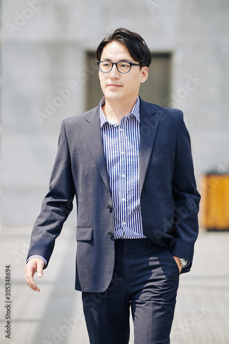 Confident Asian businessman in suit and glasses walking in the street