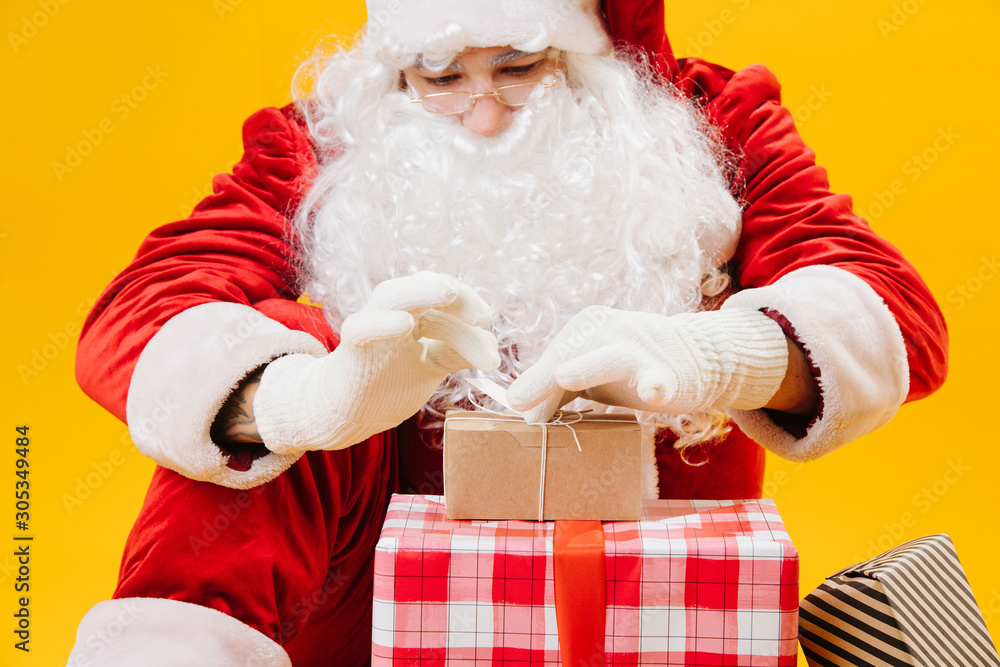 Santa Claus sitting on the floor, carefully tying little present in front of him Santa Claus sitting on the floor, carefully tying little present in front of him
