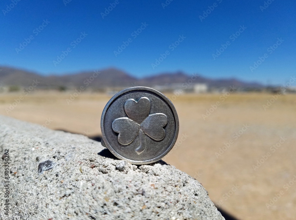 Three leaf clover silver coin balancing on rock with twin peak mountain top in the background on a sunny bright day. Three leaf clover silver coin balancing on rock with twin peak mountain top in the background on a sunny bright day.