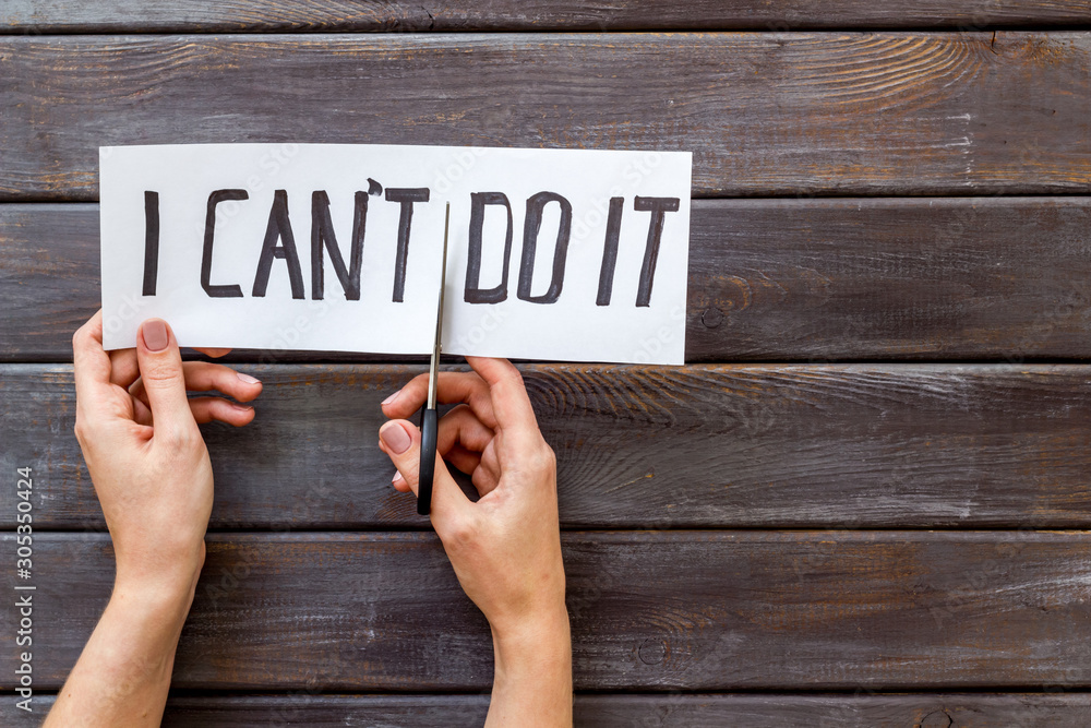 Motivation to self-developing. Hands cutting text I can't do it with scissors on dark wooden desk copy space Motivation to self-developing. Hands cutting text I can't do it with scissors on dark wooden desk copy space
