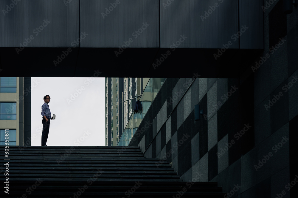Ambitious Asian entrepreneur standing on steps with cup of take away coffee in hands Ambitious Asian entrepreneur standing on steps with cup of take away coffee in hands