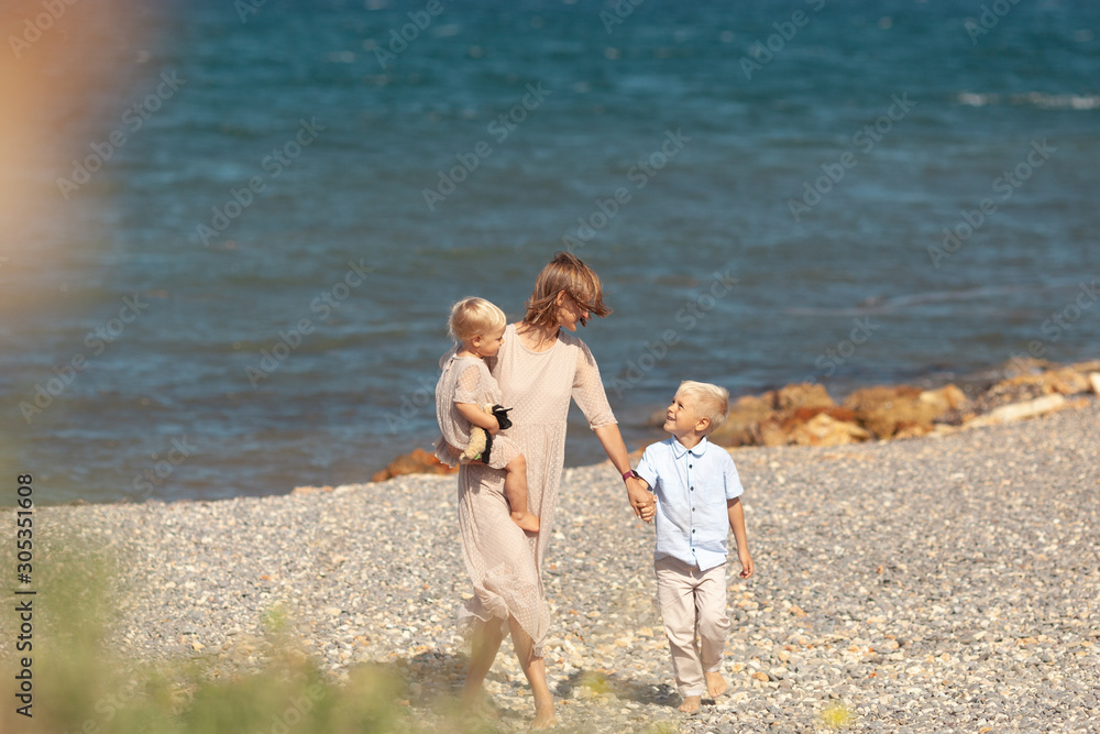 Pretty happy mom and little children on a walk near the sea