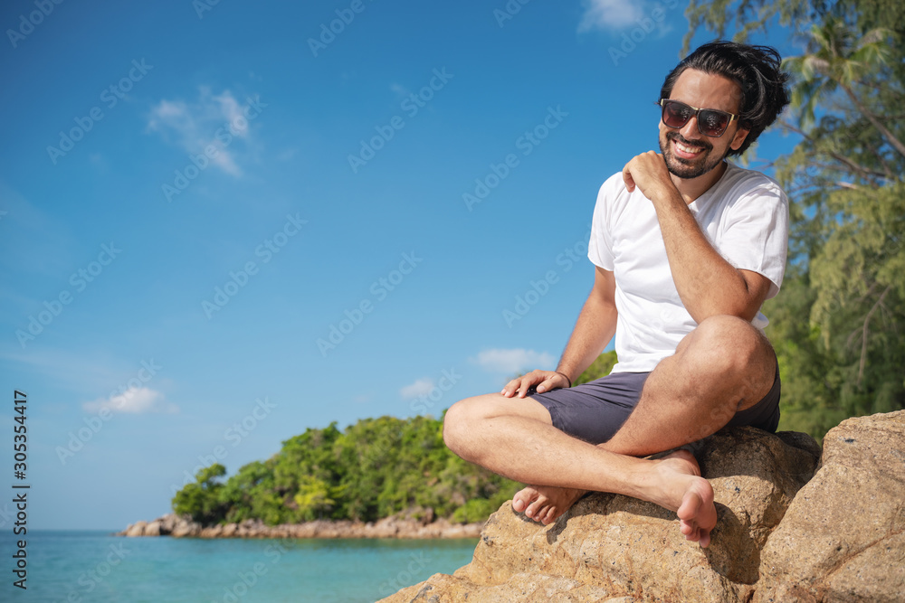 Young fashionable stylish handsome latin man in a white t-shirt and sunglasses on a bright tropical beach, vacation and travel to tropical countries Young fashionable stylish handsome latin man in a white t-shirt and sunglasses on a bright tropical beach, vacation and travel to tropical countries