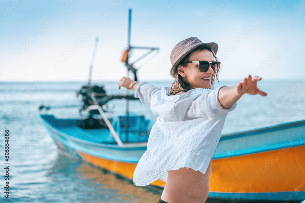 Young beautiful woman in a white shirt and sunglasses enjoys a vacation in Thailand, on the seashore against the background of a traditional Thai boat, sea travel and tours to tropical islands Young beautiful woman in a white shirt and sunglasses enjoys a vacation in Thailand, on the seashore against the background of a traditional Thai boat, sea travel and tours to tropical islands