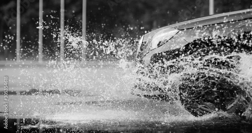 A large stream of spray erupts from under the wheels, flying far around. Black and white color grading. Slow mo, slo mo, slow motion, high speed camera Phantom photo