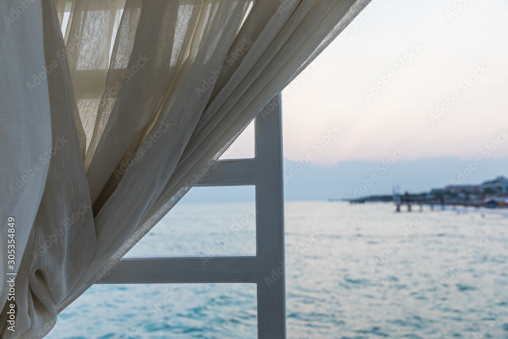 beige curtain on the background of the beach of the Mediterranean Sea at sunset