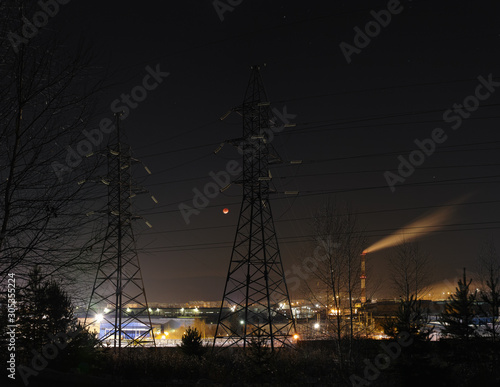 Night industrial landscape with a power line in the foreground in the background of a lunar eclipse, panorama. High resolution and detail.