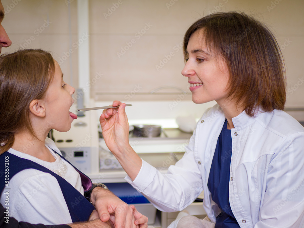 Fototapeta premium Female doctor looking at the throat of a girl patient. ENT clinic scene
