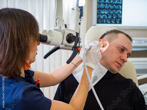 Male patient at the reception in the ENT clinic. Female doctor is cleaning ear. Theme of health, prevention and the profession of medic