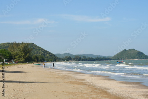 The white wave bubbles in the green water splash the brown sand  Travelers man and a woman and the dog are walking on beach  Sea with  mountain and blue sky at Khao Sam Roi Yot National Park  Thailand