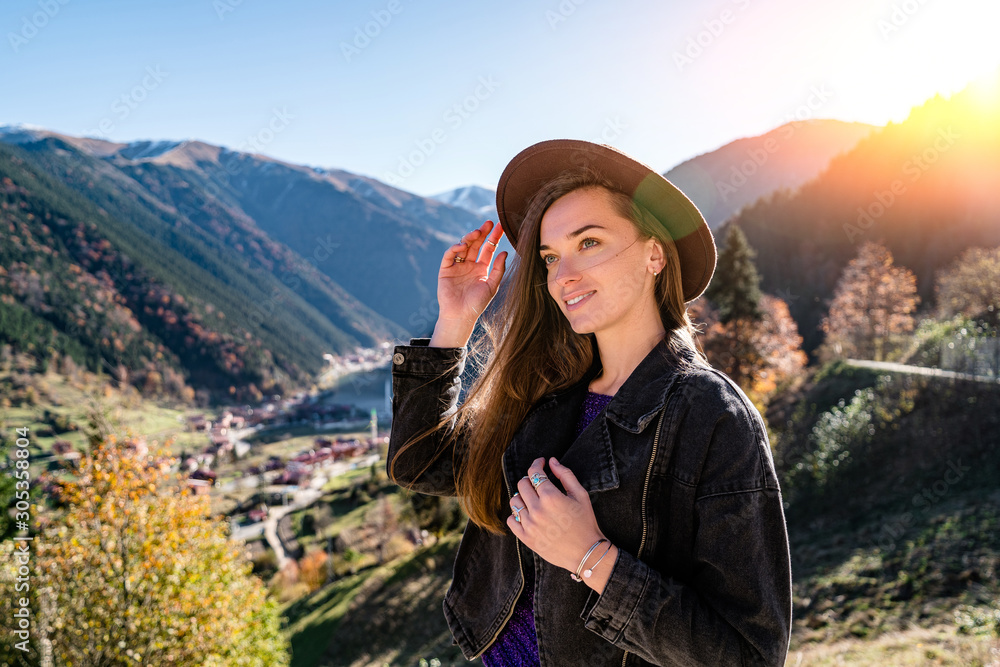 Portrait of happy smiling attractive woman traveler in a felt hat and a black denim jacket stands on the background of the mountains during Turkey travel