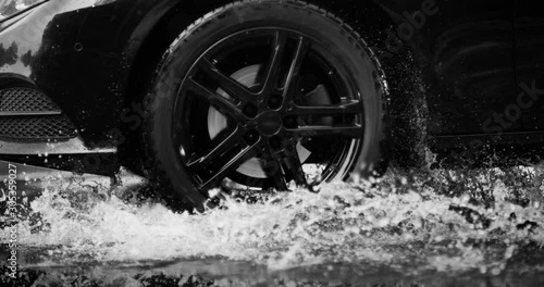 A large stream of spray erupts from under the wheels, flying far around. Black and white color grading. Slow mo, slo mo, slow motion, high speed camera Phantom