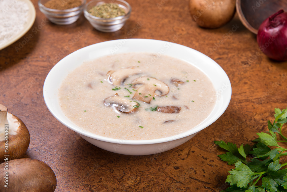  Cream mushroom soup in a white bowl on a brown background with ingredients. Selected focus.