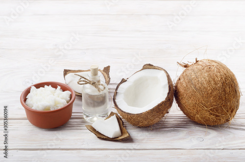 Background of coconut, coconut shell, oil in clay bowl and glass jar on white wooden table