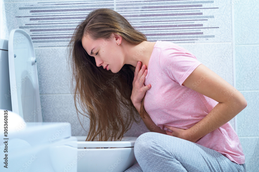 A young woman suffers from nausea and vomiting due to digestive and stomach problems. Morning toxicosis in early pregnancy. Food poisoning and infection A young woman suffers from nausea and vomiting due to digestive and stomach problems. Morning toxicosis in early pregnancy. Food poisoning and infection