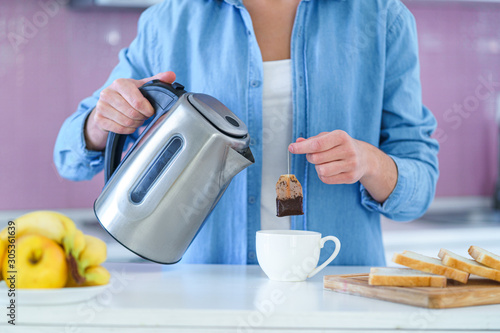 Billede på lærred Woman putting tea bag in a cup and using an electric kettle for brewing hot tea