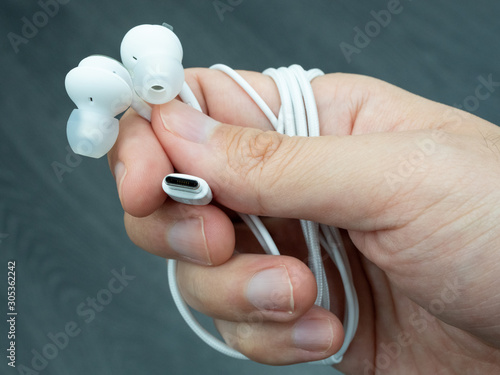 Hand holding a pair of USB-C earphones against a dark background