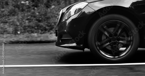 Reflecting everything around with its glossy surface, the premium car rides asphalt road where you can observe the suspension and how the tires perceive driving conditions. Black and white color photo