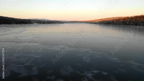 Aerial, low, drone shot, over the frozen surface of the snowless lake Kesankijarvi,, at dusk, on a sunny, autumn evening, in Pallas-yllastunturi national park, Lapland, Finland photo