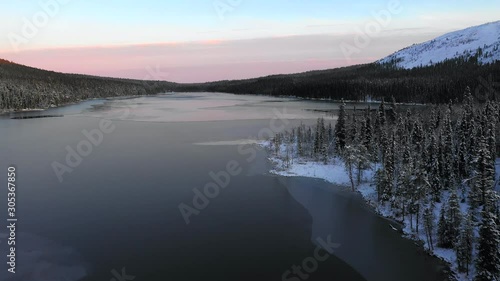 Aerial, rising, drone shot, over frozen, snowless lake Kesankijarvi, overlooking first snow on trees and the reflecting surface, at dusk, in Pallas-yllastunturi national park, Lapland, Finland photo