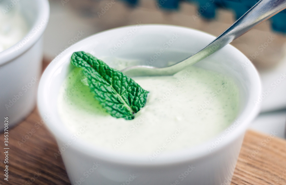White yogurt sauce with mint in small whire bowl for traditional meze dinner on the wooden table in restaurant. White yogurt sauce with mint in small whire bowl for traditional meze dinner on the wooden table in restaurant.