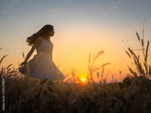 Trendy girl in stylish summer dress feeling free in the field with flowers in sunshine,enjoying nature, Beautiful Teenage Model in the Spring Field, Sun Light.