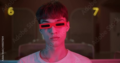 Portrait of Cool Millenial Guy Wearing Party Trendy Glasses Turning Head and Looking Straight to Camera with Futuristic Neon Lighting Numbers at the Background. Close Up shot. photo