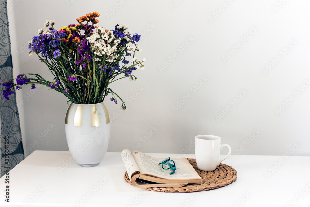 bouquet of flowers, open book and glasses, lemon tea in a white ceramic cup on a wicker stand on the table, cozy home interior. bouquet of flowers, open book and glasses, lemon tea in a white ceramic cup on a wicker stand on the table, cozy home interior.