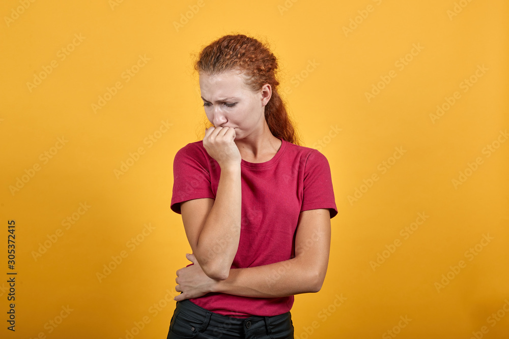 Scared young lady in red shirt keeping hand on mouth, looking nervous isolated on orange background in studio. People sincere emotions, health concept. Scared young lady in red shirt keeping hand on mouth, looking nervous isolated on orange background in studio. People sincere emotions, health concept.